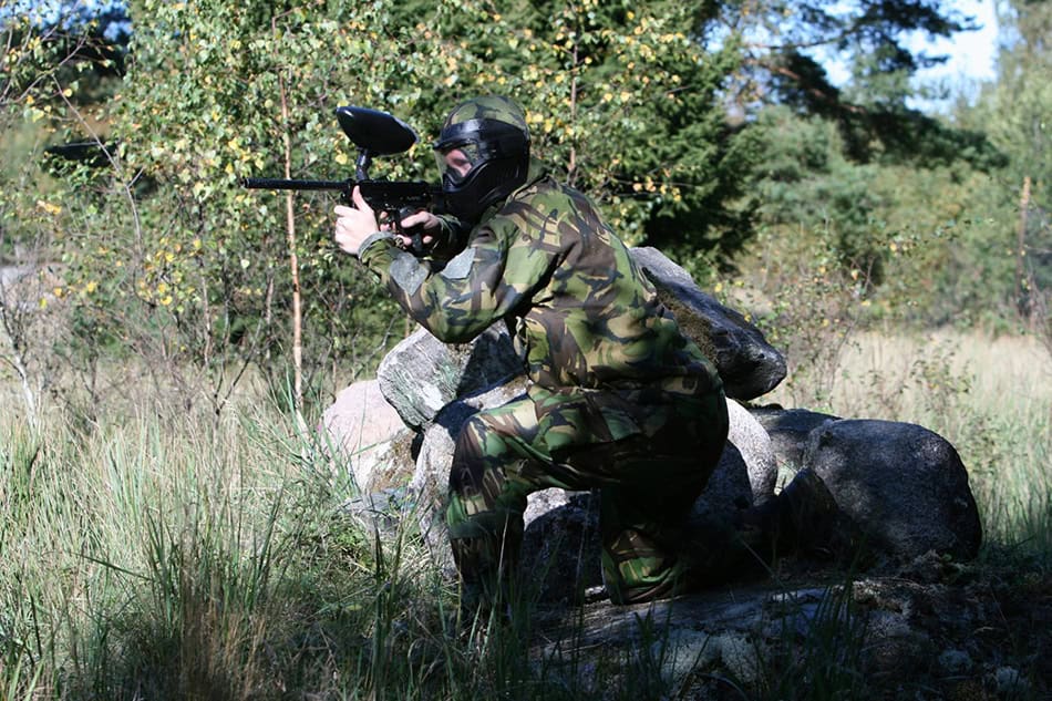 Person klädd i kamouflage står med paintball geväret redo att skjuta.