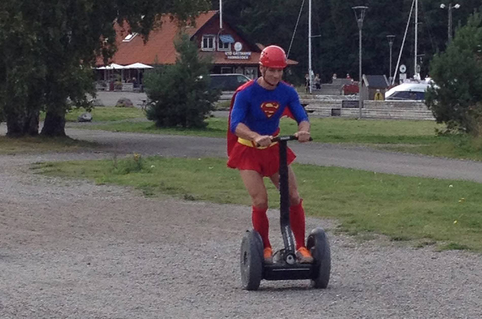 En man i superman klädsel åker fram på en segway.