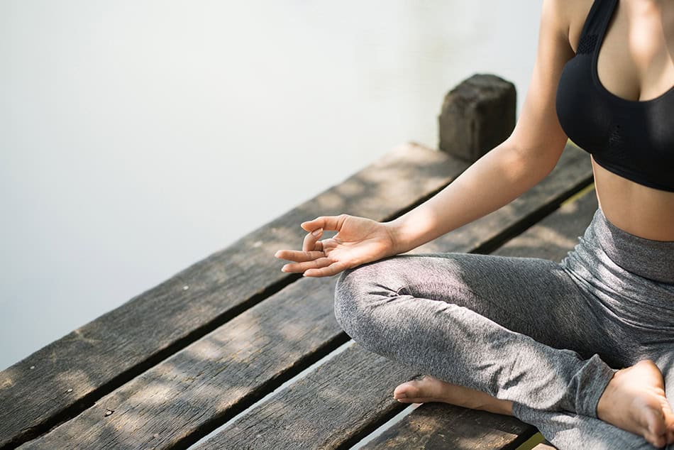 En kvinna sitter på en brygga och utövar yoga.